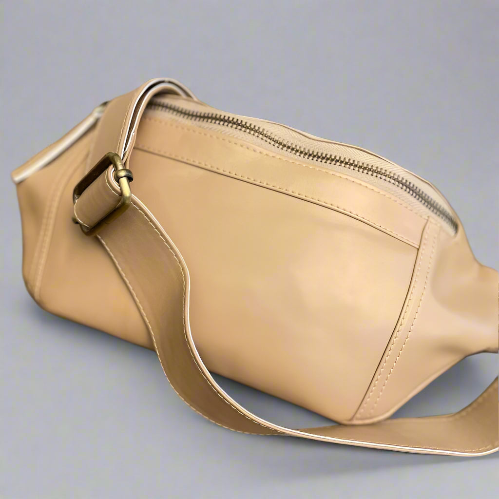 A beige vegan leather sling bag with a shoulder strap and two zippered compartments