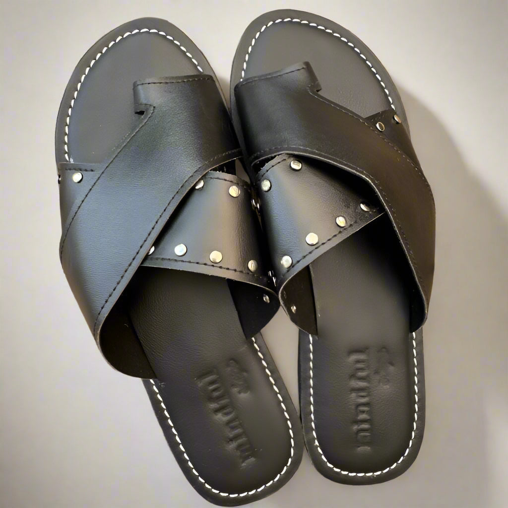 A pair of black vegan slides with silver studs on a wooden surface.