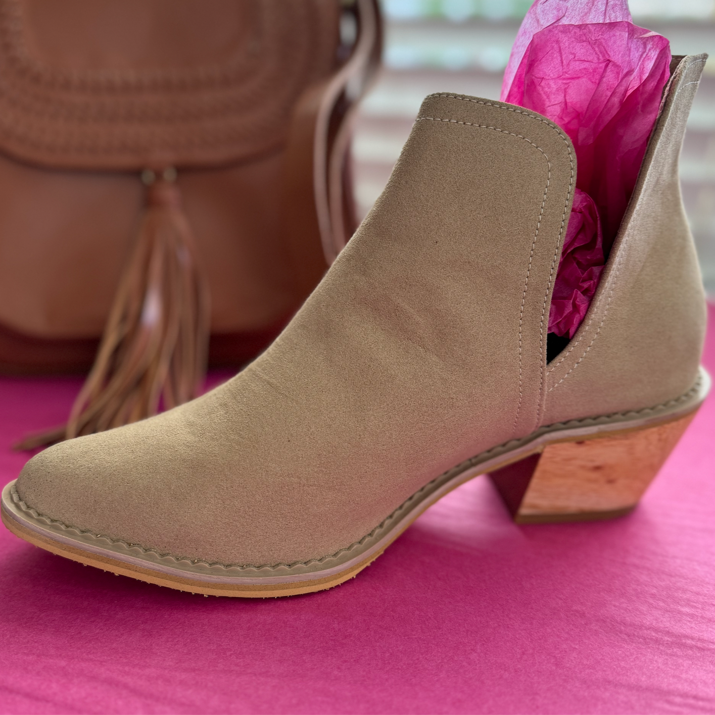 Beige ankle boot with wooden heel on a pink surface, with a brown bag in the background.