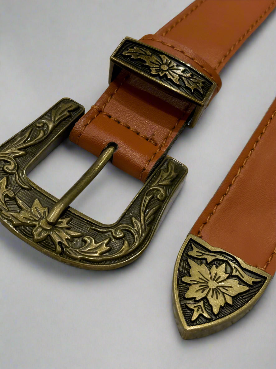 A vegan leather western belt with a black strap and a silver-colored ornate buckle, on a dark background.