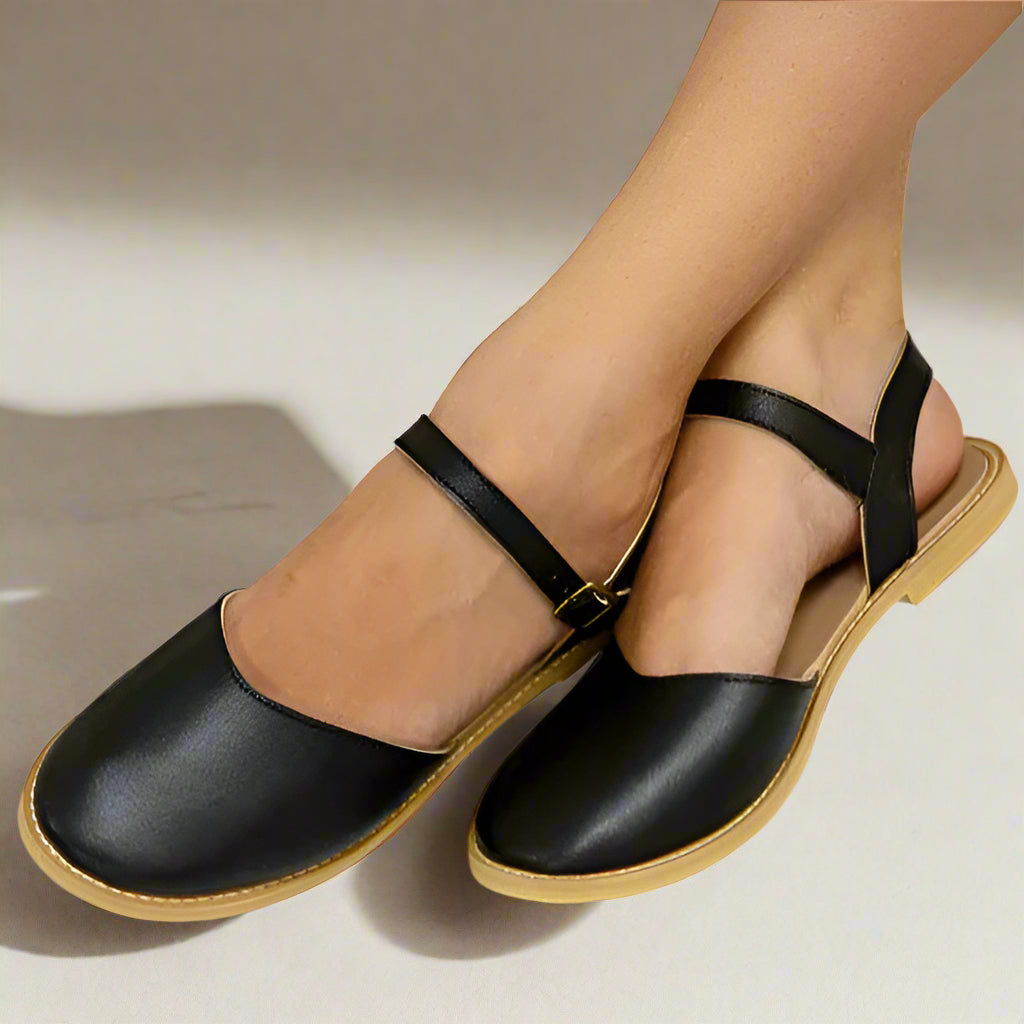 A pair of black vegan leather sandals with a buckle closure on the ankle