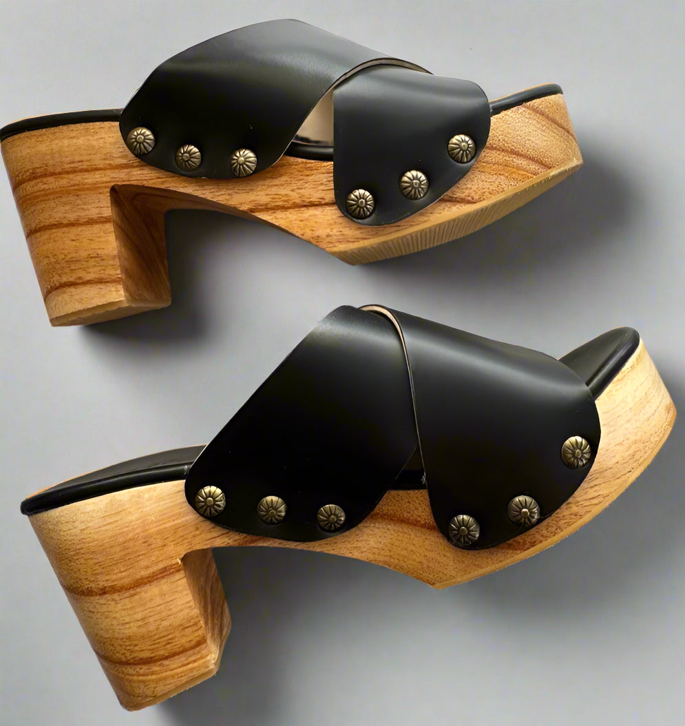 Pair of wooden clogs with black leather straps on a white background